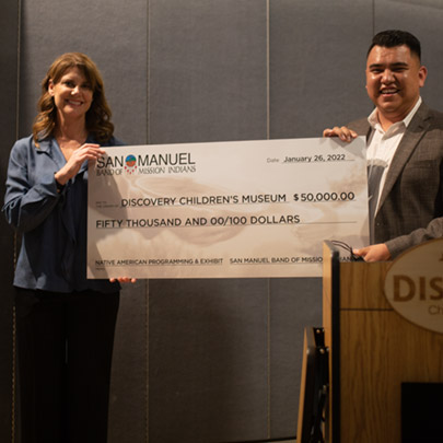 A man and woman holding an oversized check with a $50,000 donation to the Discovery Children's Museum