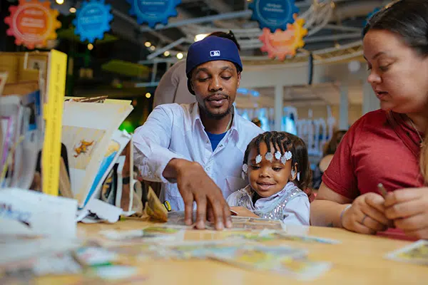 parent_resources-600 A man and woman arranging paper on a crafts table with a child at the Discovery Children's Museum