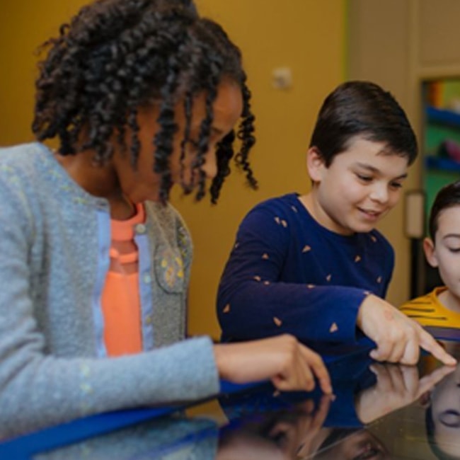 Kids pointing over a glass screen in awe