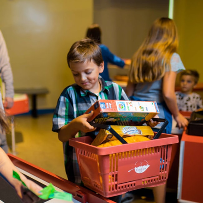 Un niño con una cesta de la compra llena de falsos comestibles