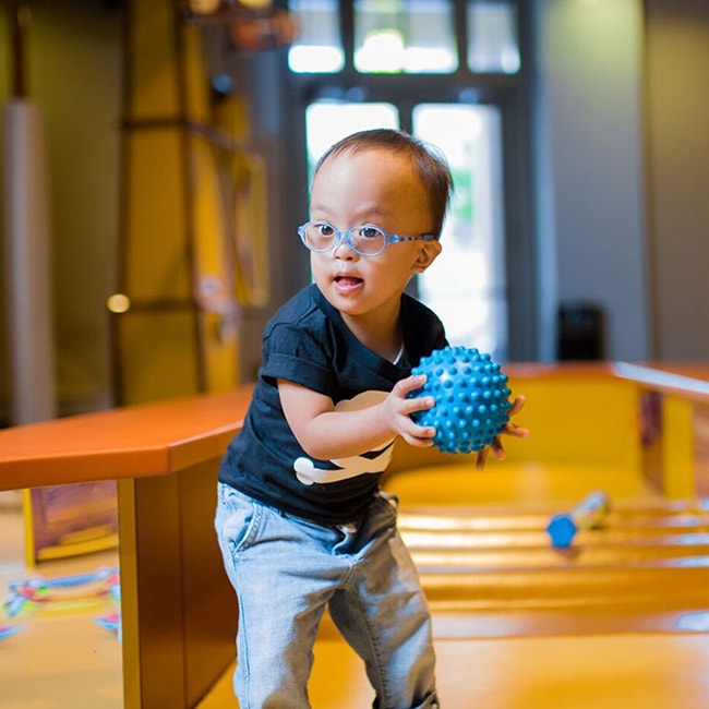 A toddler wearing glasses and holding a spiky rubber ball