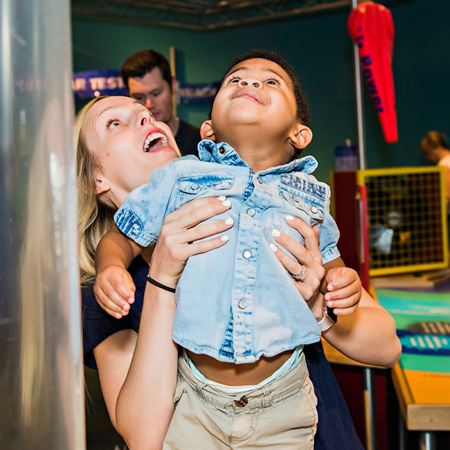 A mother and her child both looking up and the child being lifted up by her mother