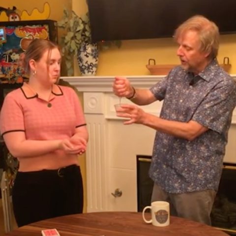 magician Mac King holding dripping liquid as he demonstrates a magic trick to a nearby woman