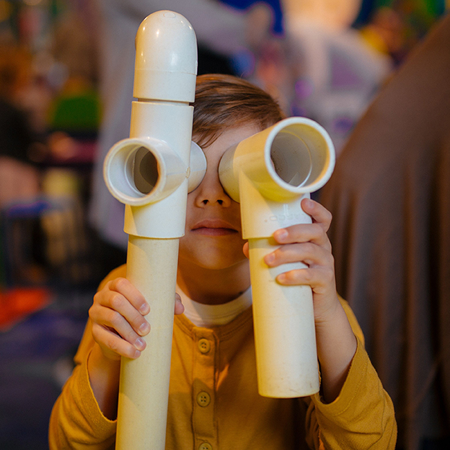 A young boy looking through two PVC pipes