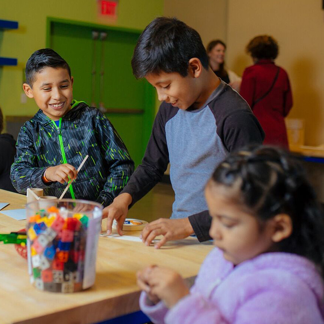 two young boys and a younger girl working on artwork on a big desk