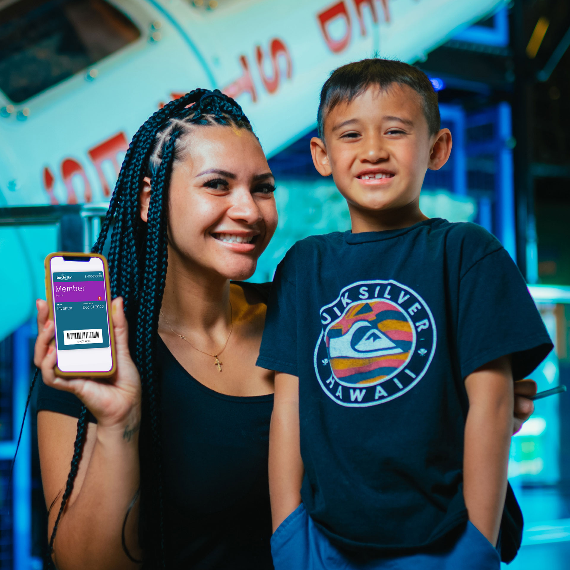 una mujer posa con su sol mientras sostiene un teléfono móvil hacia delante para mostrar la página de miembros del Discovery Children&#039;s Museum