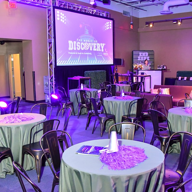 Foto de una sala del museo con mesas cubiertas con un mantel e iluminación ambiental de color púrpura.