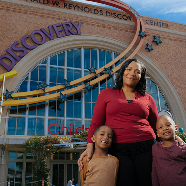 A mother standing with her two young children in front of the Discovery Kids Museum building
