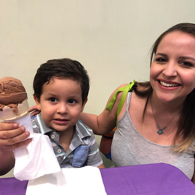 a child holding a chocolate ice cream cone sitting next to a his mother
