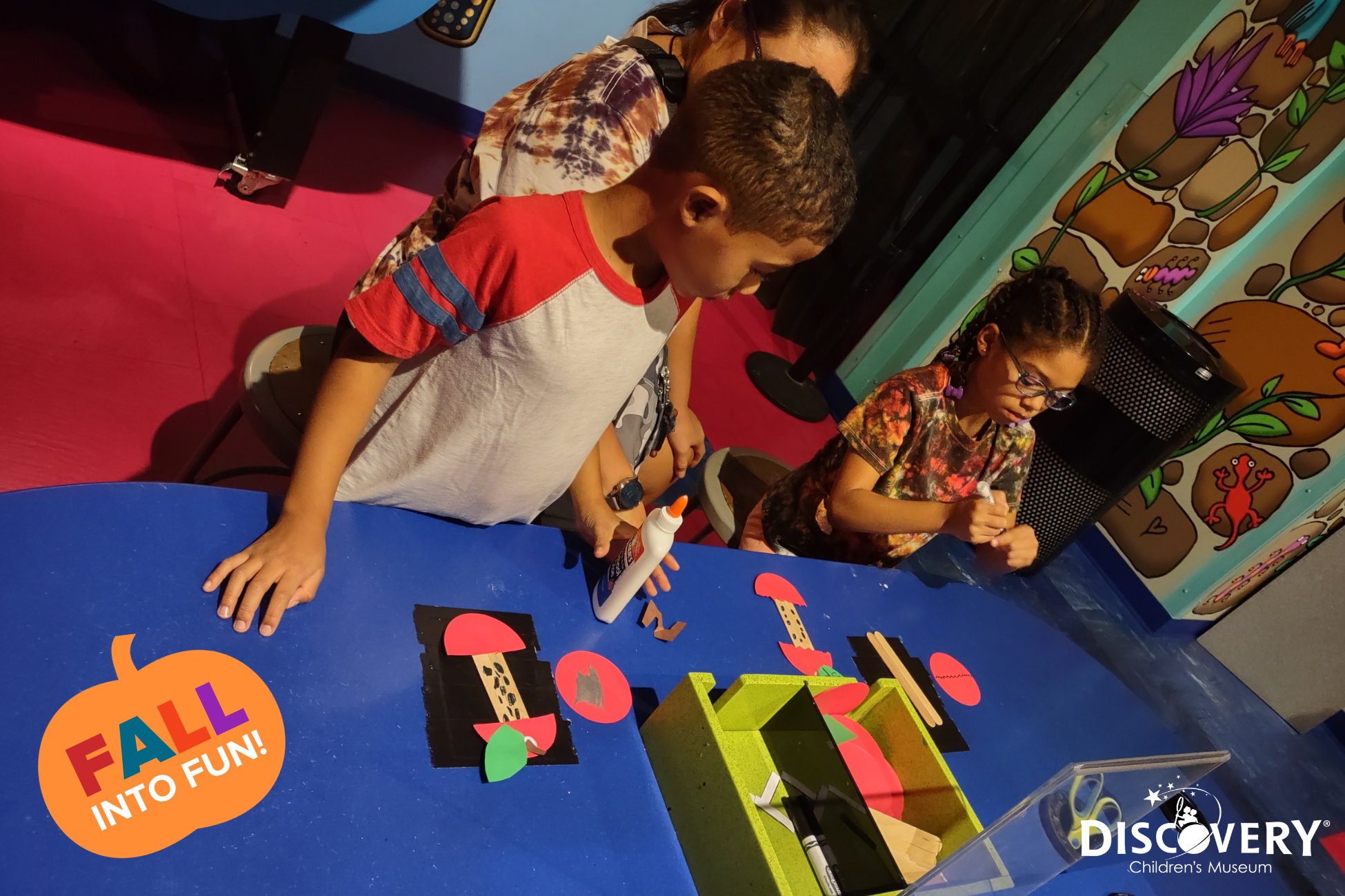 un niño haciendo manualidades de papel observa a una niña a su lado haciendo manualidades de papel en el Discovery Children&#039;s Museum