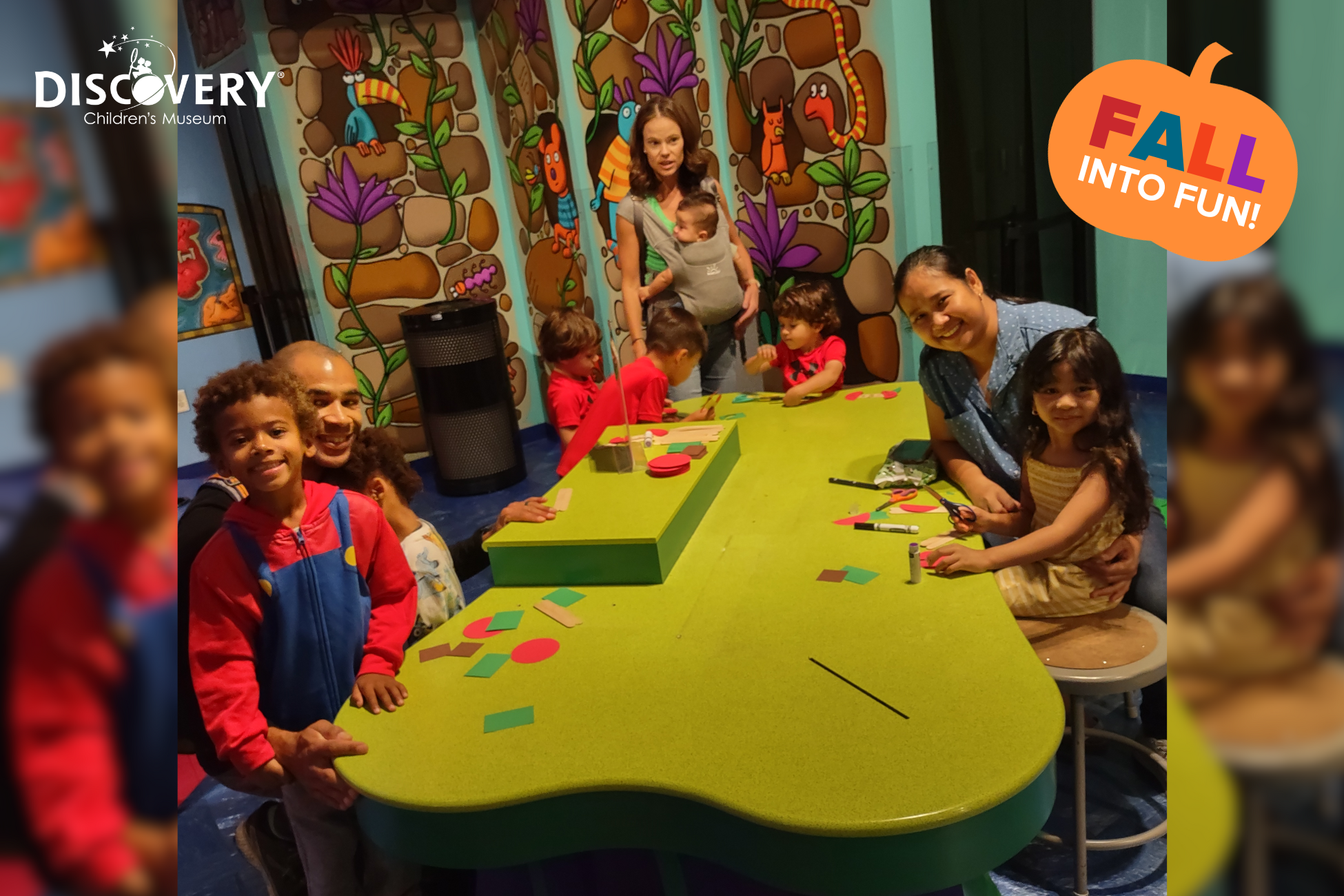 3 familias con niños pequeños en una larga mesa verde de manualidades posando para una foto en el Discovery Children&#039;s Museum