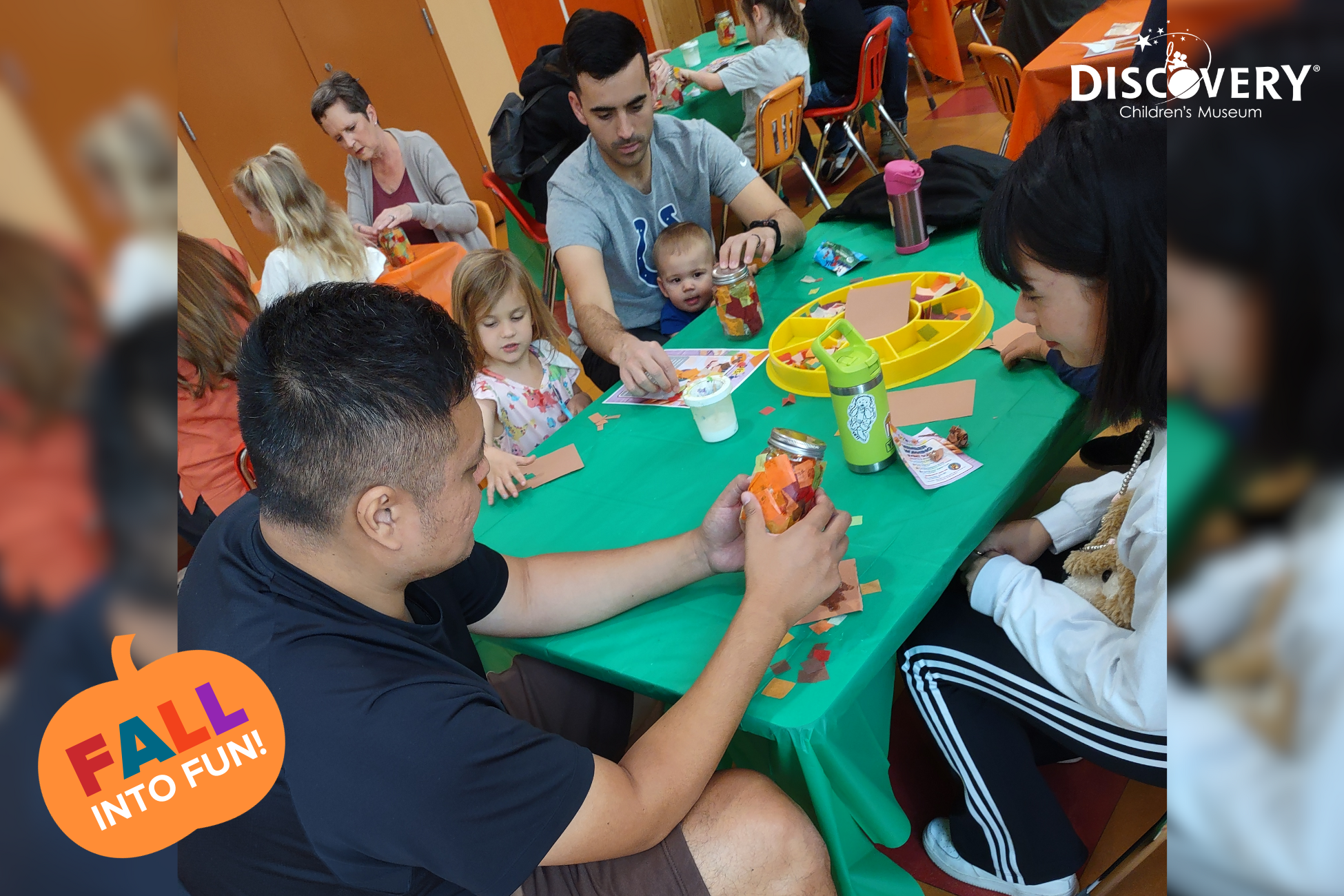 un hombre y una mujer miran un tarro lleno de restos de papel de colores en una mesa de manualidades con padres y niños en el Discovery Children&#039;s Museum