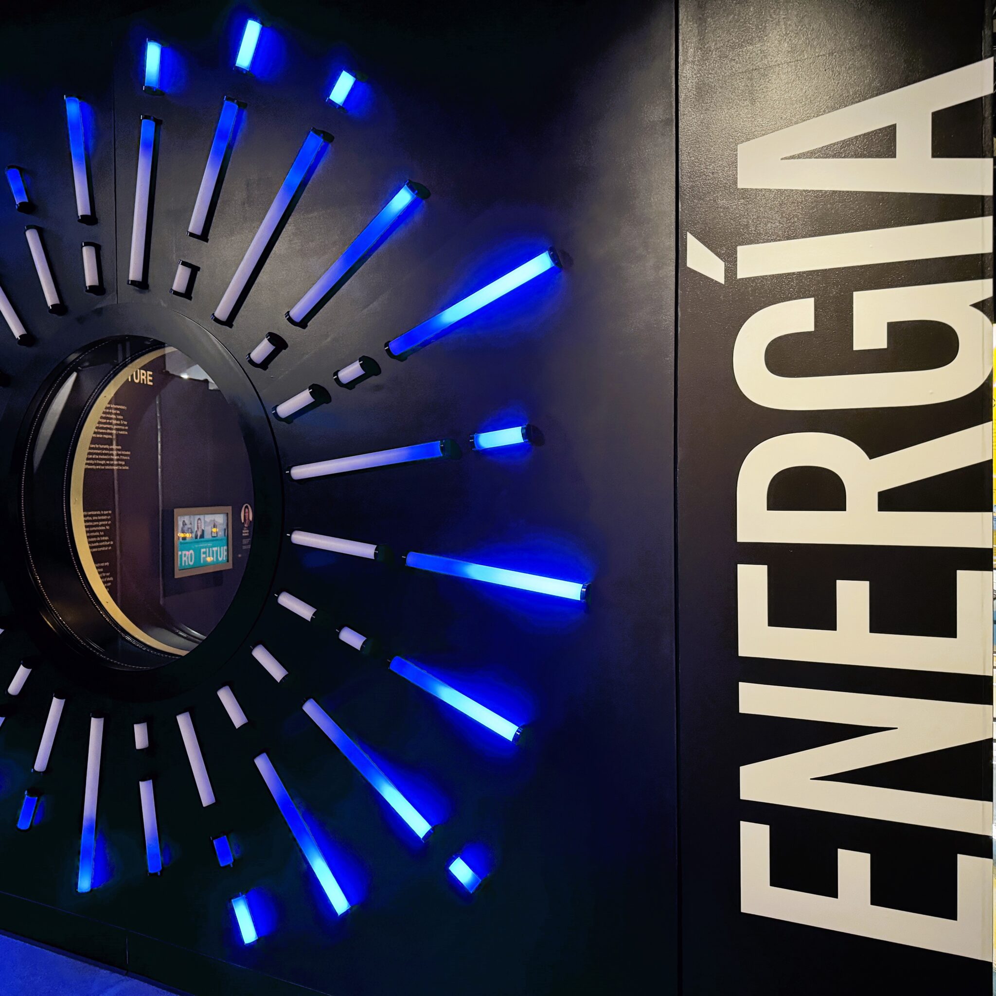 A black wall with a large circular hole surrounded by rods of light of varying lengths next to the word "ENERGÍA" at the Discovery Children's Museum