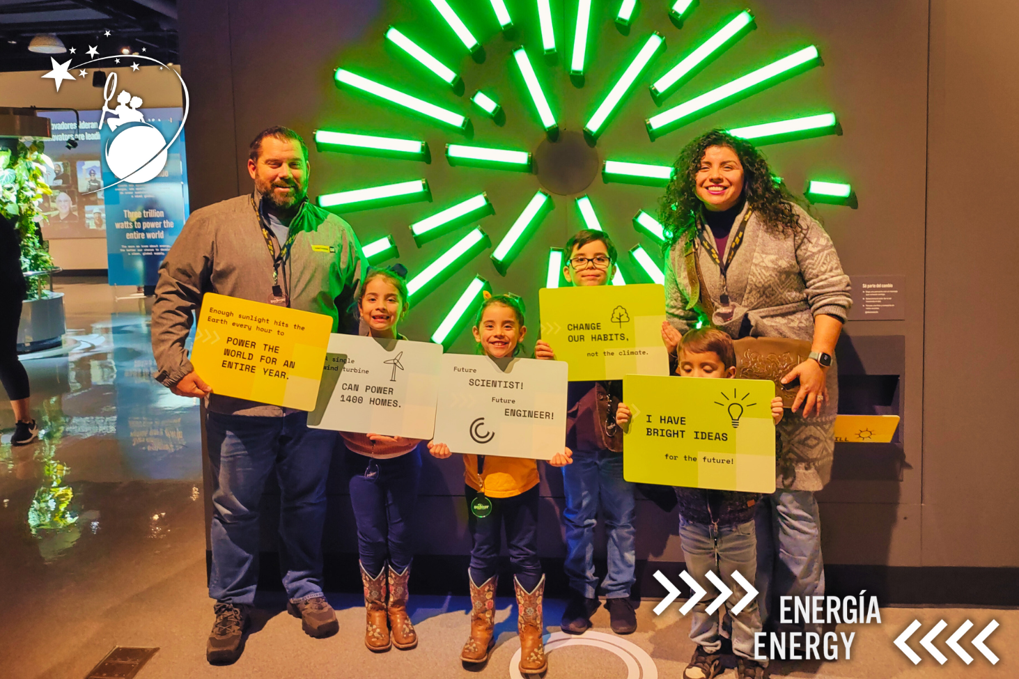 2 padres y 4 niños posan para una foto y sostienen carteles con datos y lemas escritos en ellos en el Discovery Children&#039;s Museum.