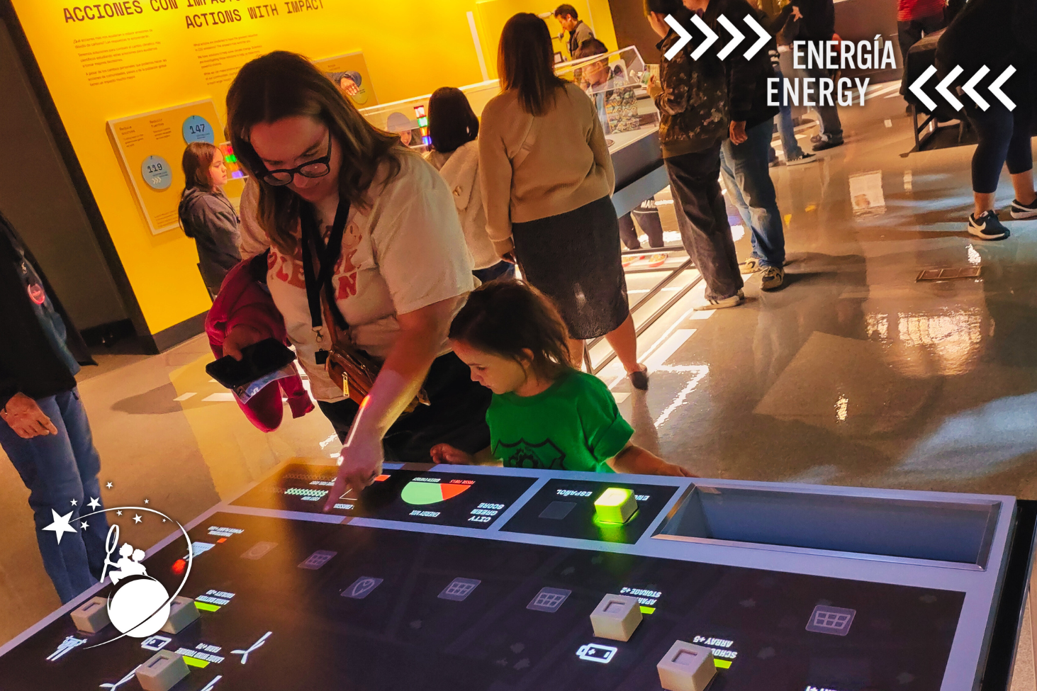 ディスカバリー子供博物館のエネルギー展示で、幼い娘にテーブルの情報を教える母親。