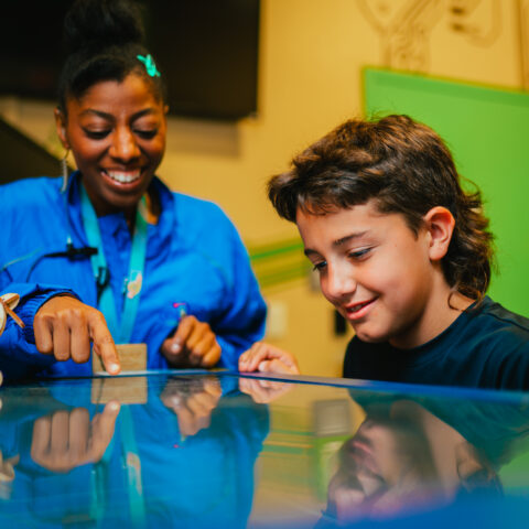 un empleado del museo señala información en una pantalla de mesa para un niño en el Discovery Children&#039;s Museum