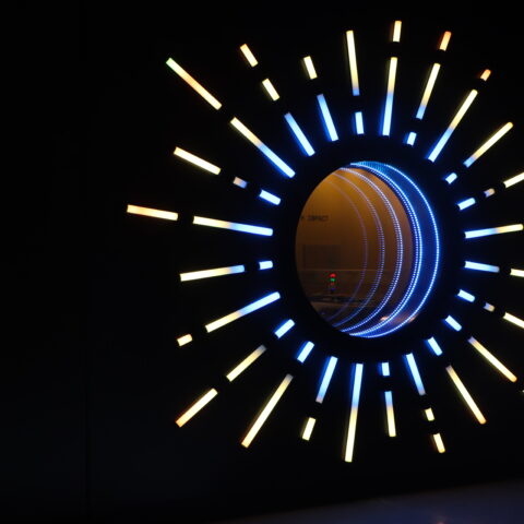 ディスカバリー・チルドレンズ・ミュージアムの「ENERGÍA」の文字の横にある、長さの異なる光の棒で囲まれた大きな円形の穴のある黒い壁。