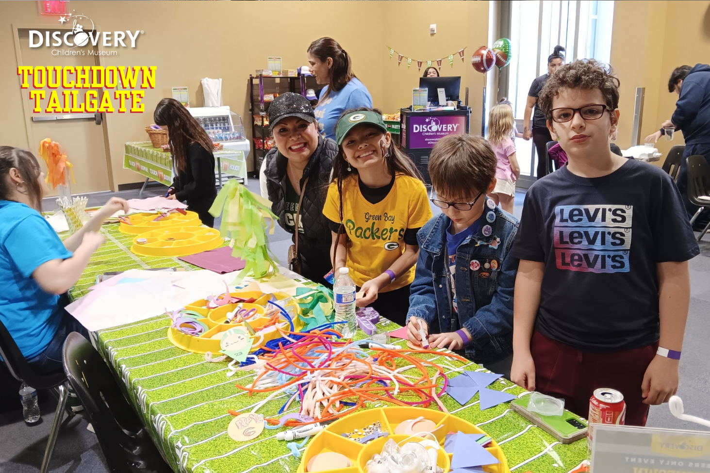 children and parents posing for a photo next to a long arts and crafts table at the Discovery Children's Museum