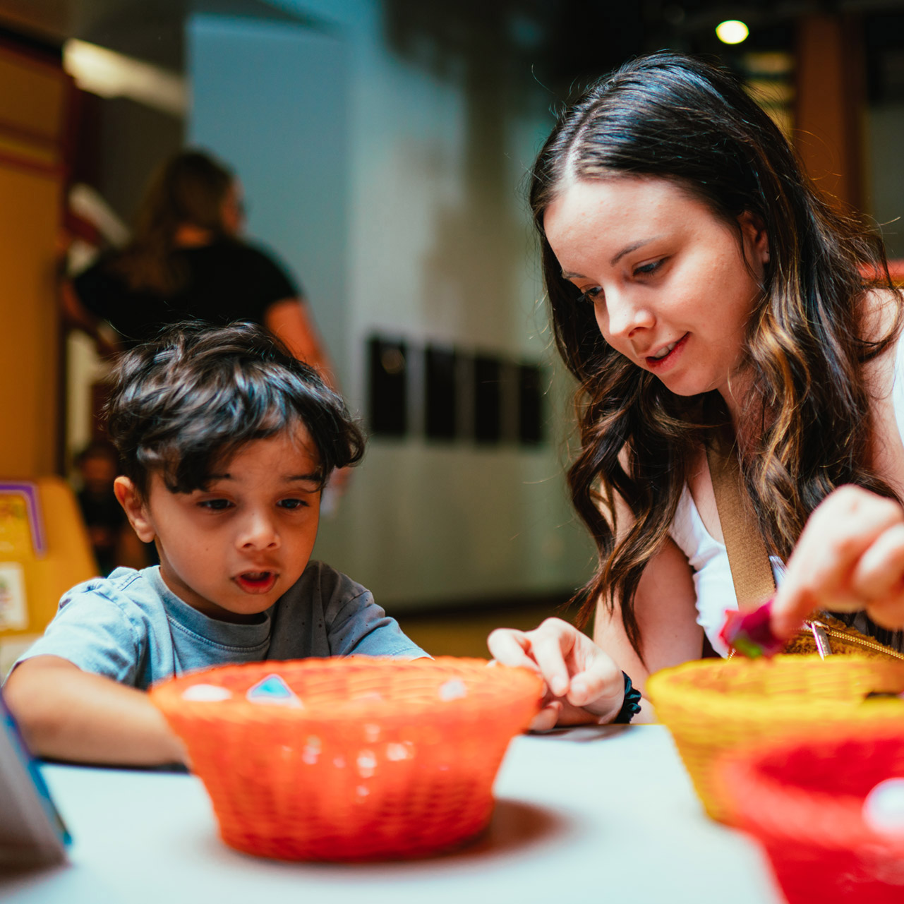 mujer sentada junto a su hijo pequeño cerca de cestas de colores con material para manualidades Discovery Children&#039;s Museum