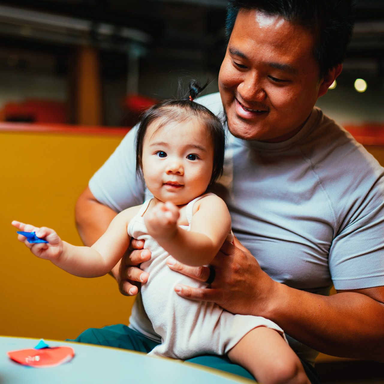 A father holds his toddler daughter while she holds paper crafts at the Discovery Children's Museum